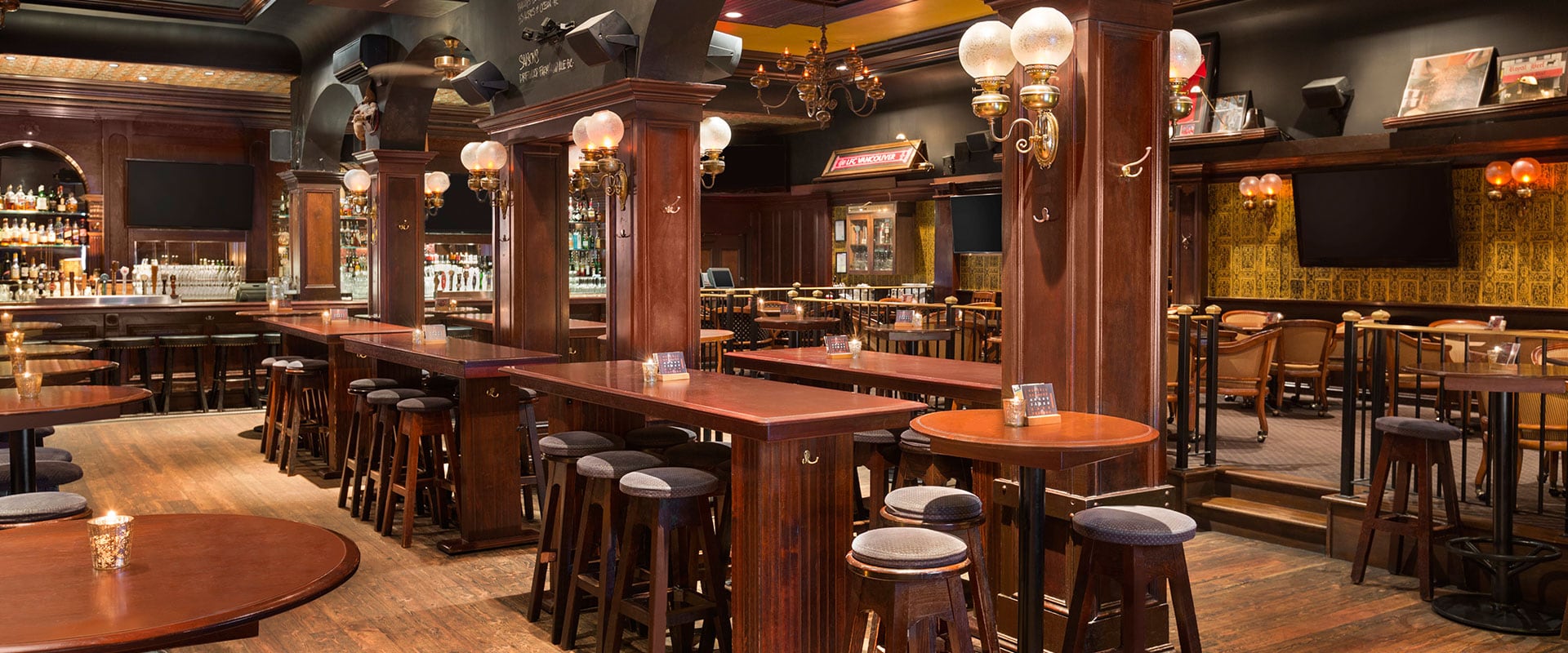 Long red-brown tables provide lots of seating with lighting from antique double glass sconces mounted on walls at the Butcher and Bullock pub in Downtown Vancouver.