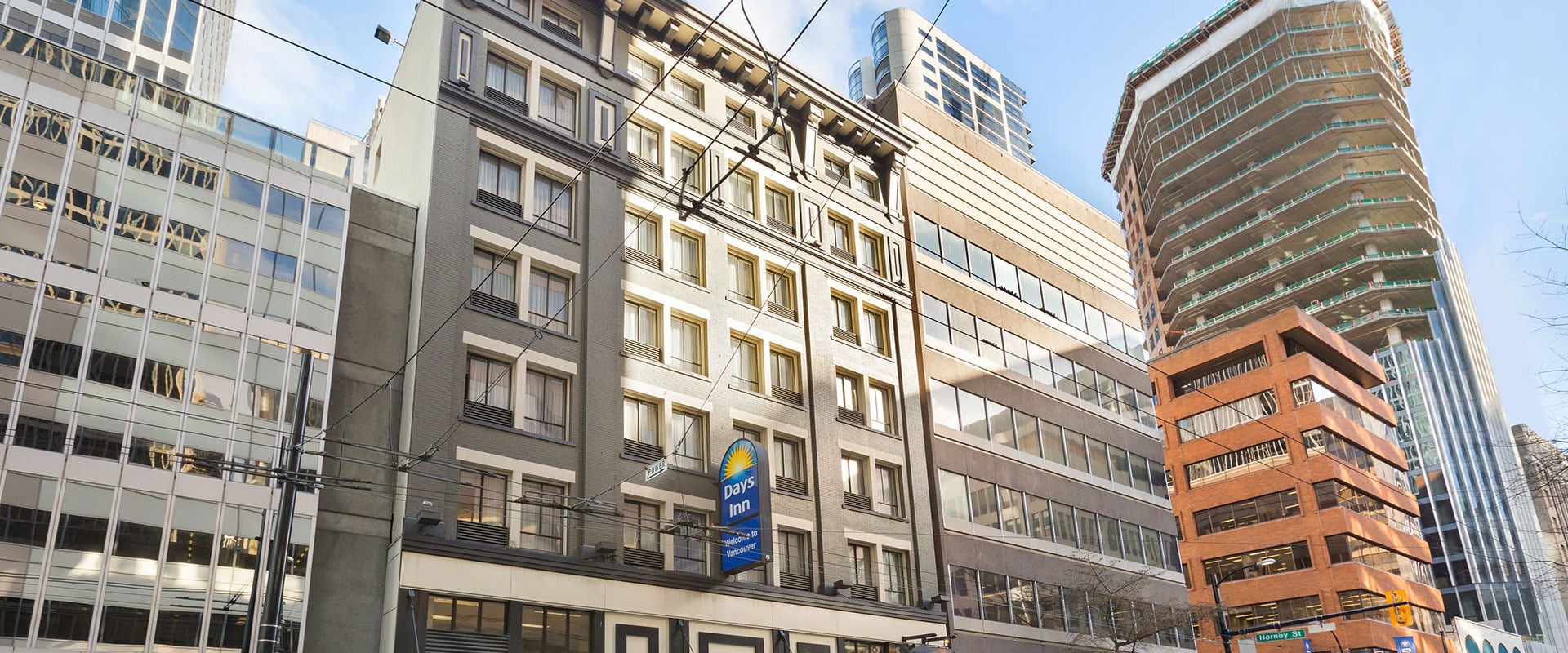 An outside view of the top storeys and windows of the Days Inn Vancouver Downtown hotel with the blue, white and yellow corporate logo sign attached to the building.