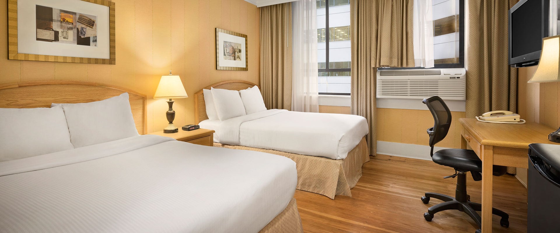 Standard Two Doubles suite at Days Inn Vancouver Downtown, features gold-yellow painted walls, two double beds, hardwood floors, a writing desk and leather padded chair.
