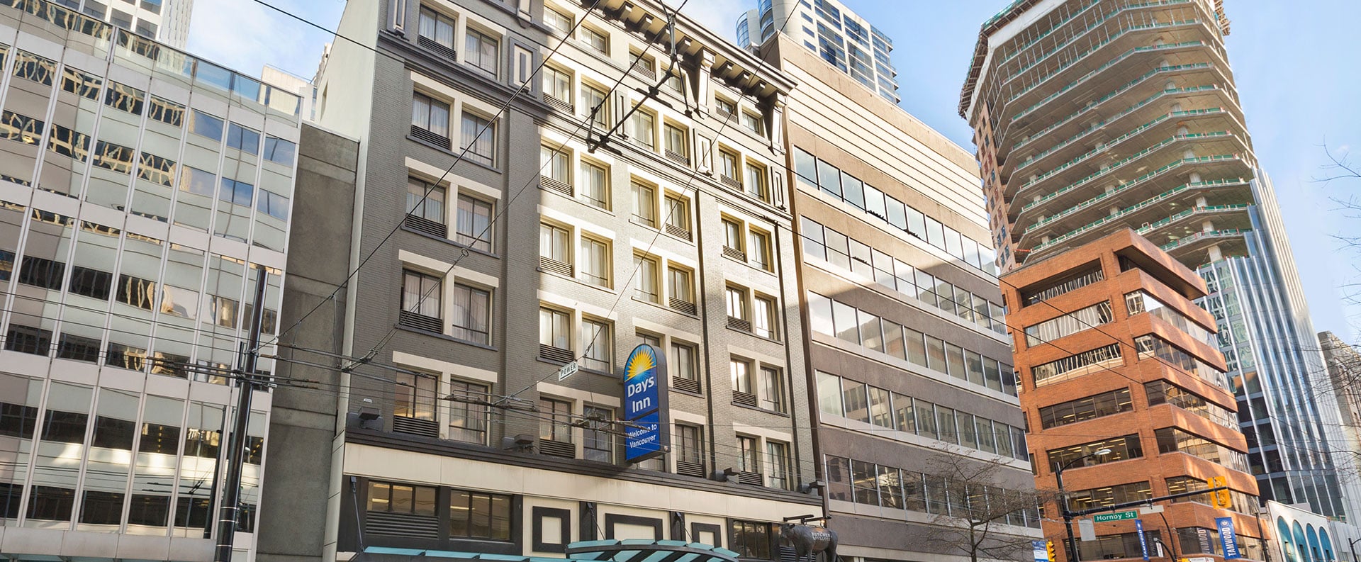 Upward view of the multi-storey Days Inn Vancouver Downtown hotel with rows of windows facing down onto Pender Street on a bright and sunny day.