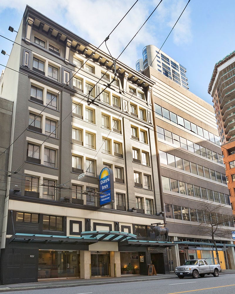 A front view of the multi-story building of Days Inn Vancouver Downtown with the corporate logo sign placed above the glass door entrance.