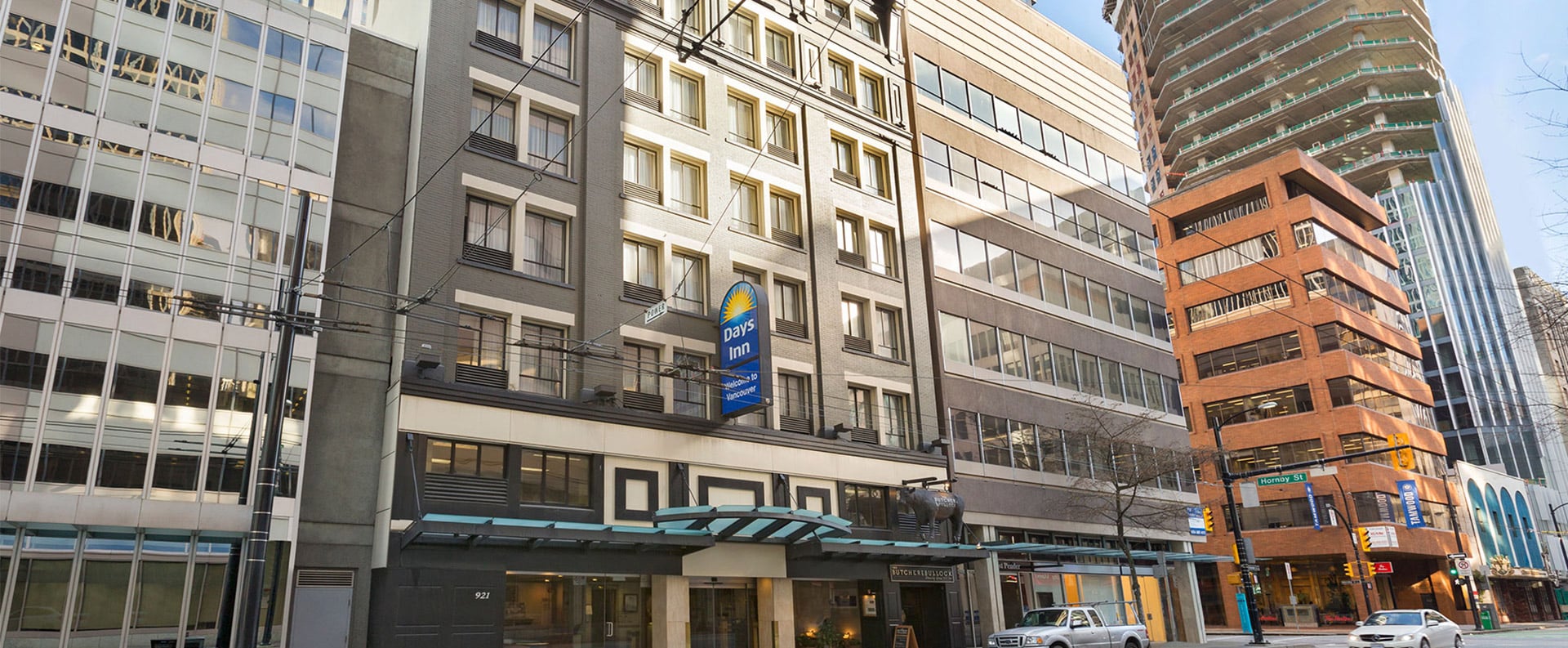 A large view of the front glass door entrance to Days Inn Vancouver Downtown with rows of windows of the hotel facing onto West Pender Street.